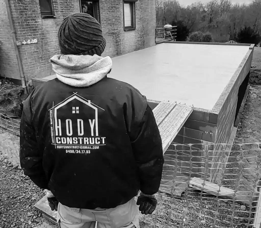Florent Hody, de dos, en veste Hody Construct devant une dalle de béton en cours de réalisation (photo en noir et blanc)