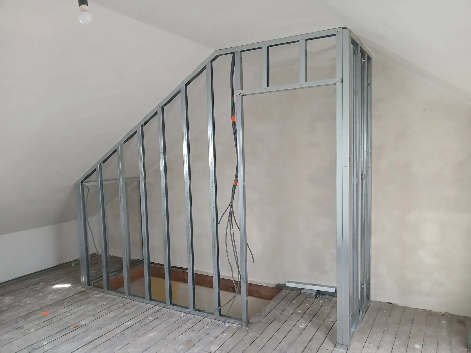 Ossature métallique d'une cloison sous la pente du toit d'un grenier, plancher en planches