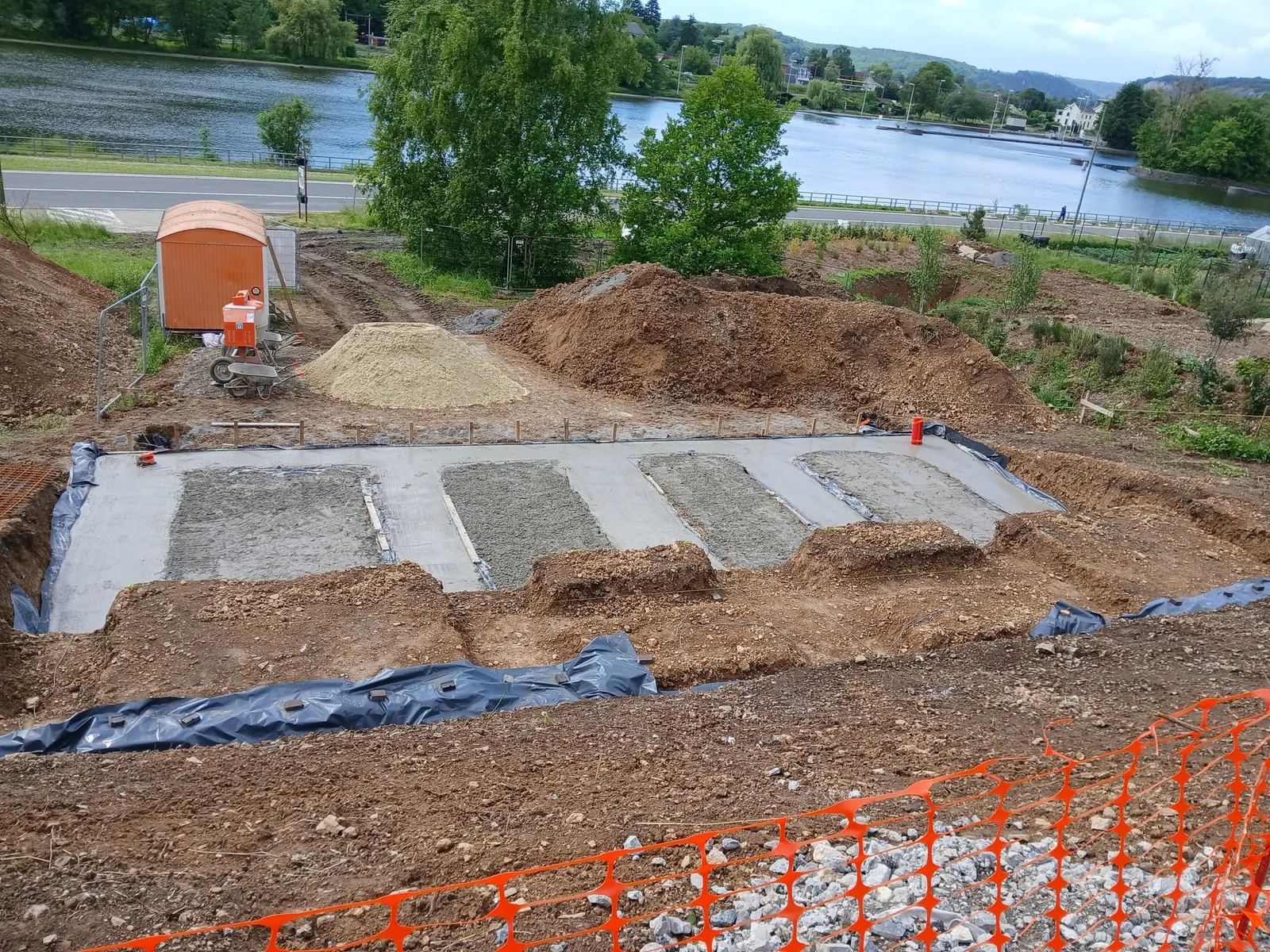 Dalle de fondation coulée par bandes sur un terrain terrassé, membranes noires sur les côtés et lac à l'arrière-plan