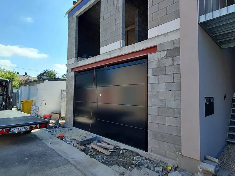 Façade d'un bâtiment neuf en blocs avec porte de garage noire et balcon