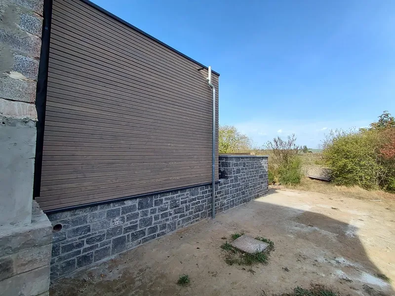 Façade en bardage bois sur un muret de pierre bleue, ciel bleu