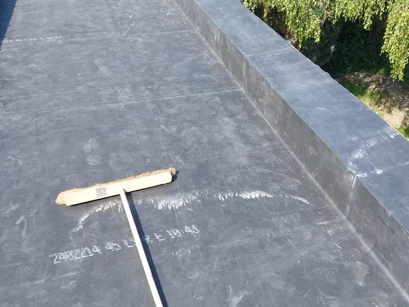 Toiture plate recouverte d'une membrane noire avec relevés, un balai posé en travers