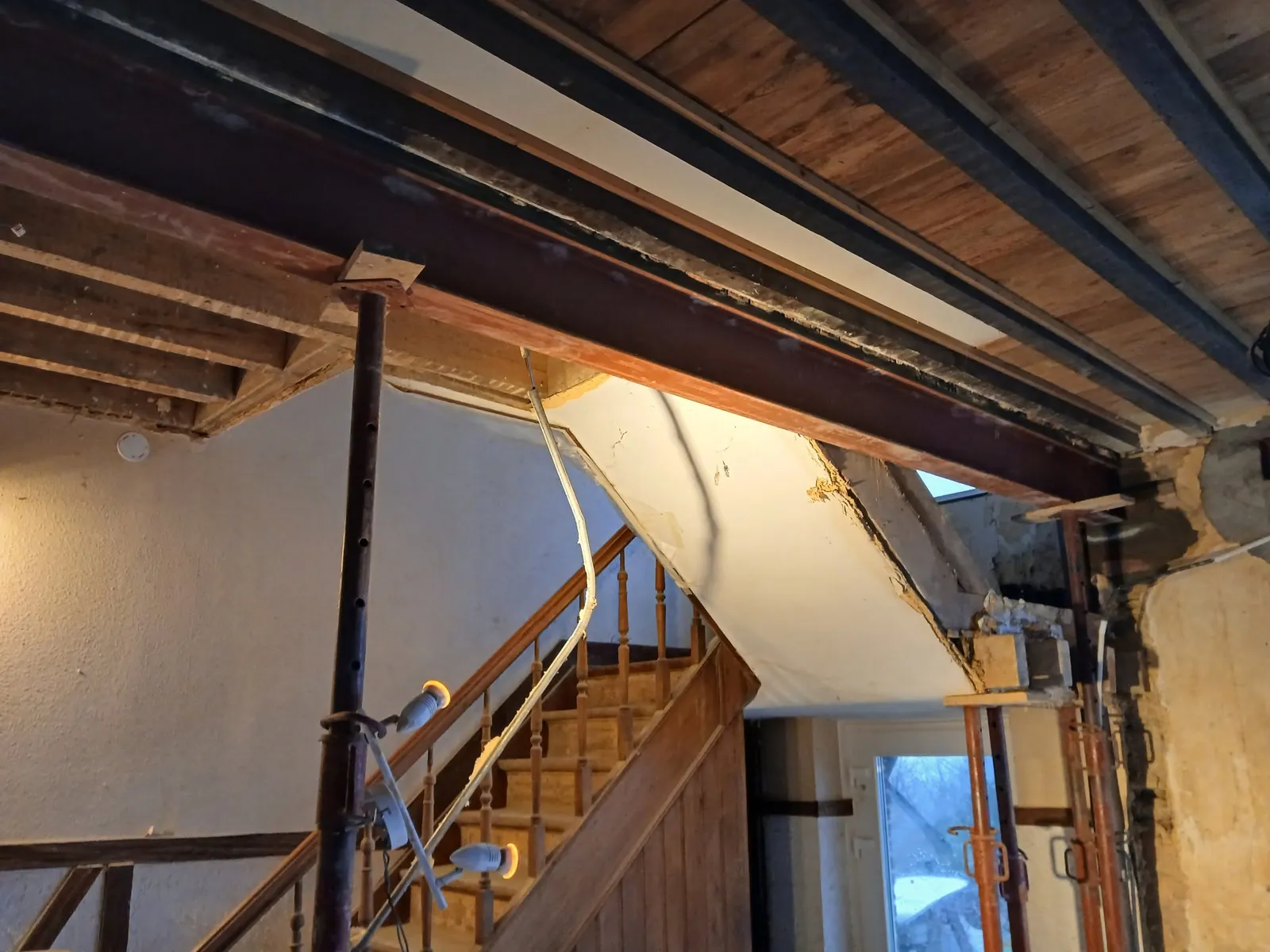 Poutre en acier calée sur un étai au-dessus d'un escalier en bois, plafond à solives apparentes