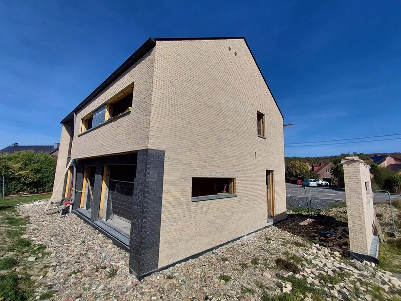 Maison en briques beige avec soubassement noir, ciel bleu