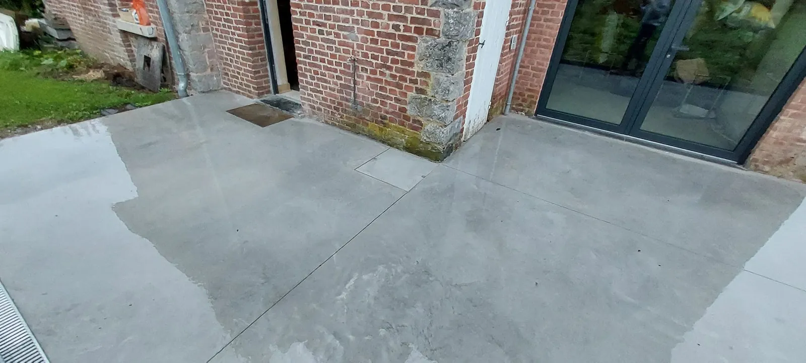 Terrasse en béton lissé devant une façade en briques et une porte-fenêtre noire