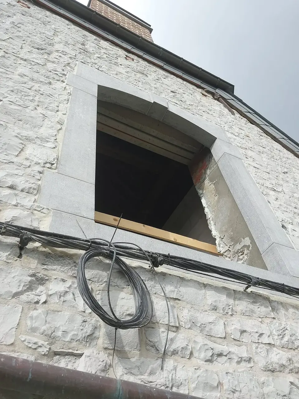 Ouverture de fenêtre encadrée de pierre bleue sur façade en moellons