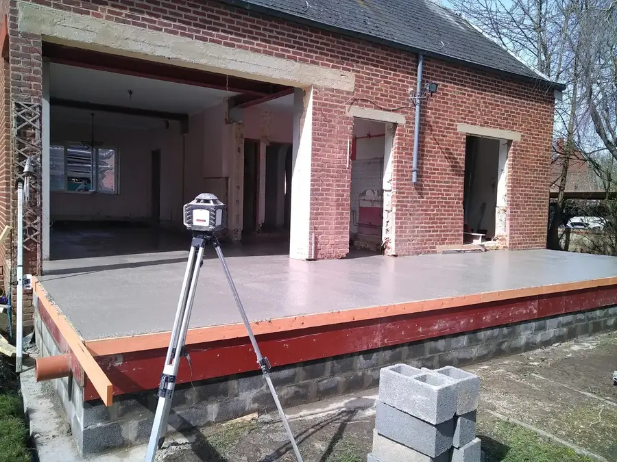 Dalle de béton devant une maison en briques avec grande ouverture
