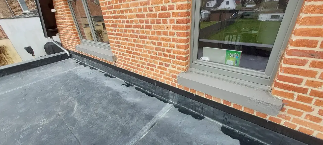 Toiture plate terminée contre la façade en briques