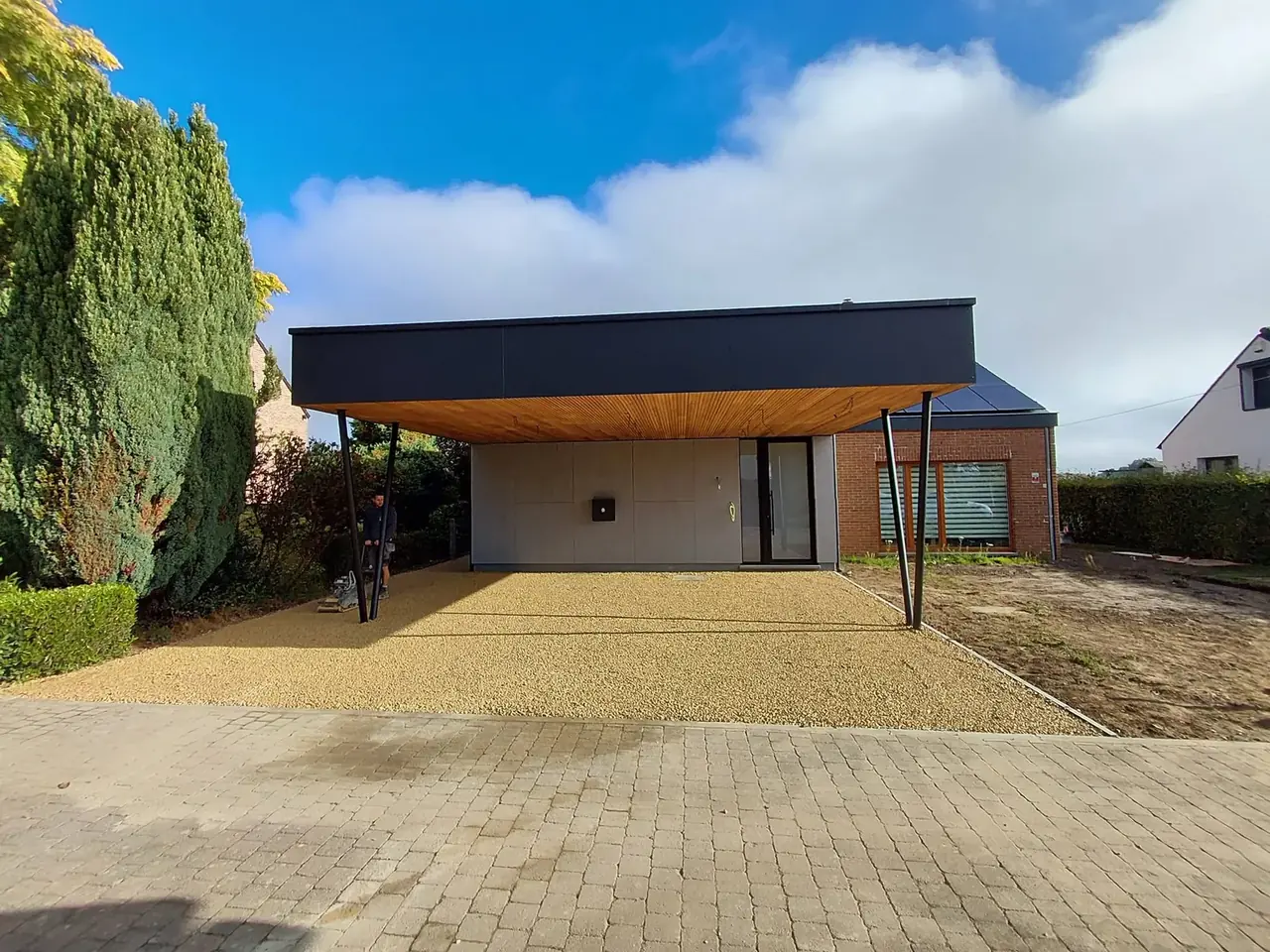 Carport avec toit plat bordé de noir et allée en gravier