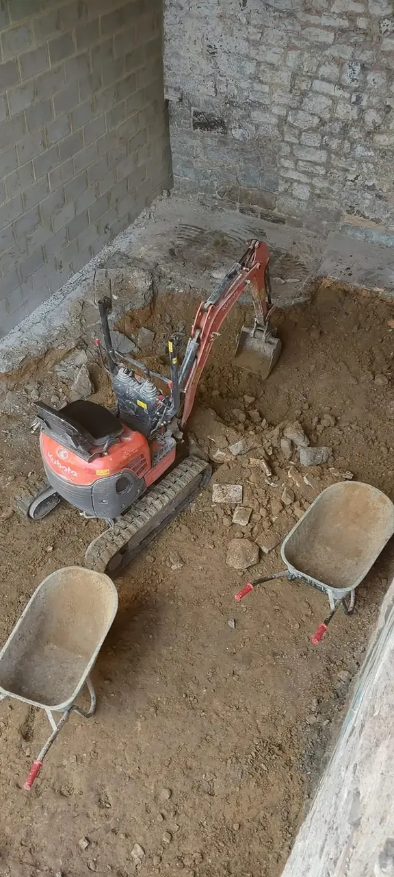 Mini-pelle dans une fouille entre des murs de pierre et de blocs