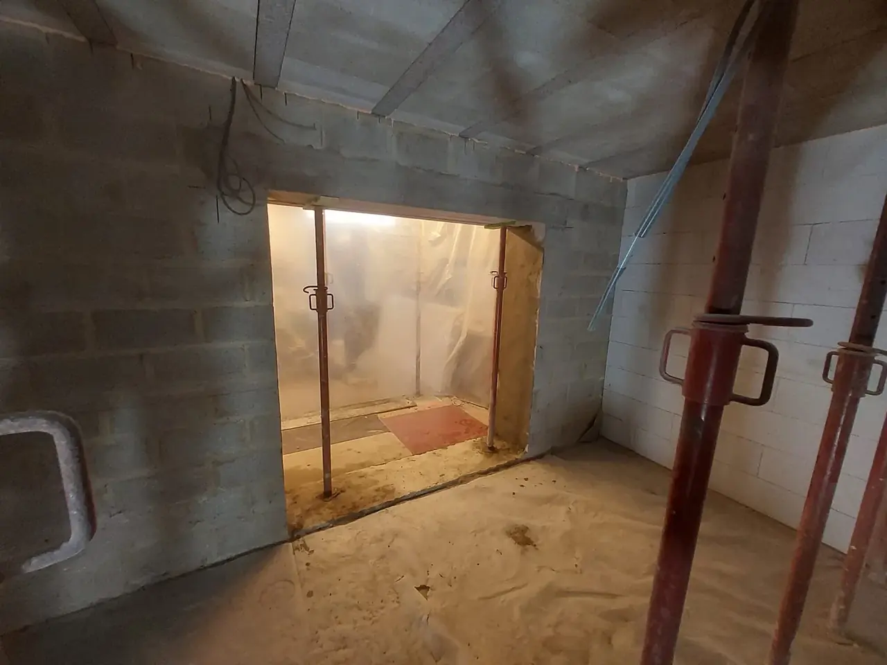 Ouverture dans un mur de blocs avec étais vers la pièce voisine