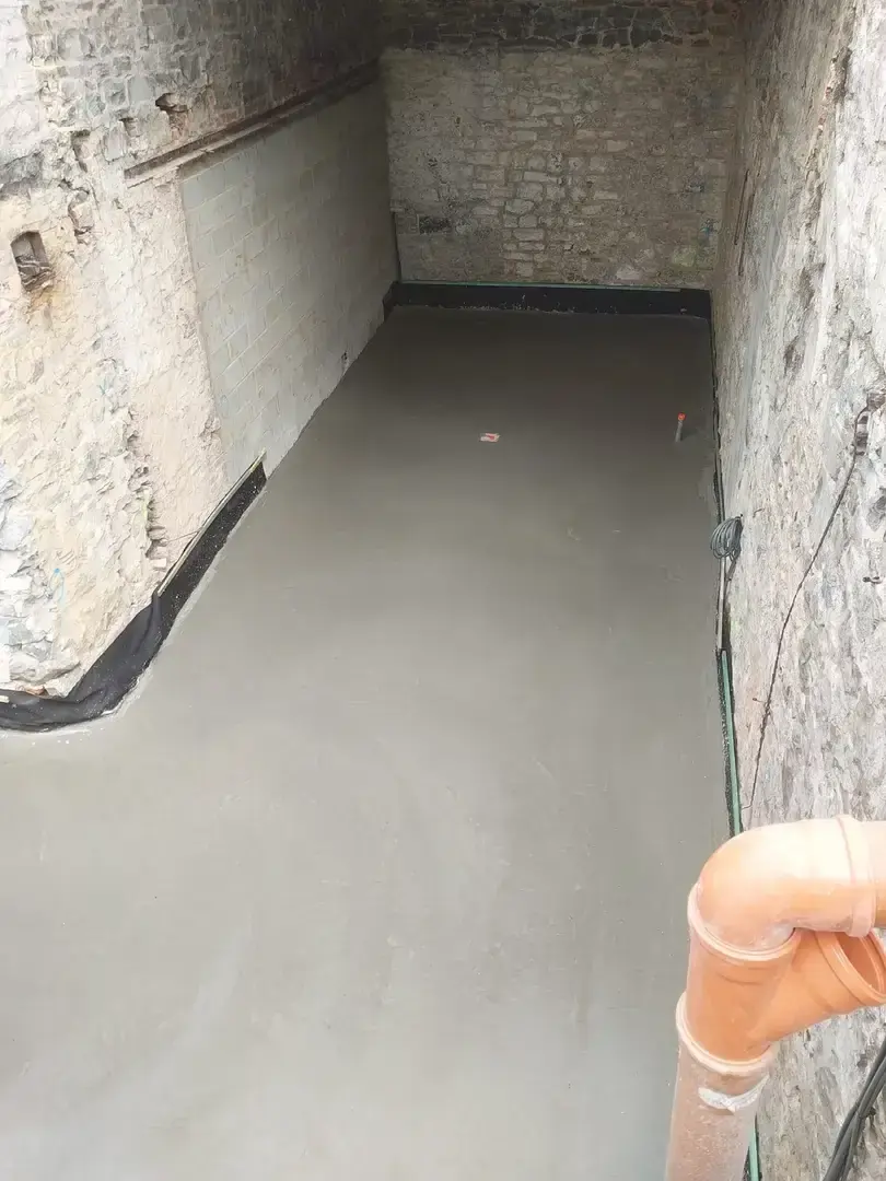 Dalle de béton brut dans une pièce voûtée en pierre avec tuyau orange