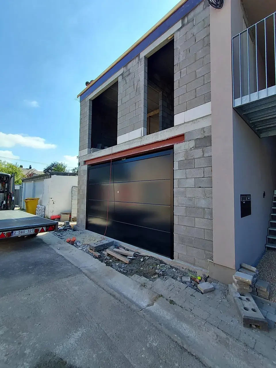 Façade du bâtiment avec porte de garage noire et balcon