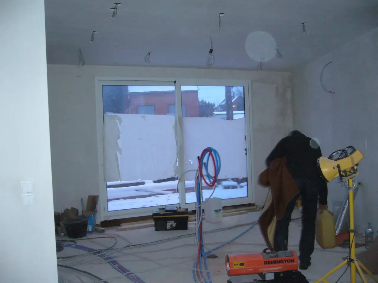 Ouvrier de dos devant une baie vitrée dans une pièce en travaux