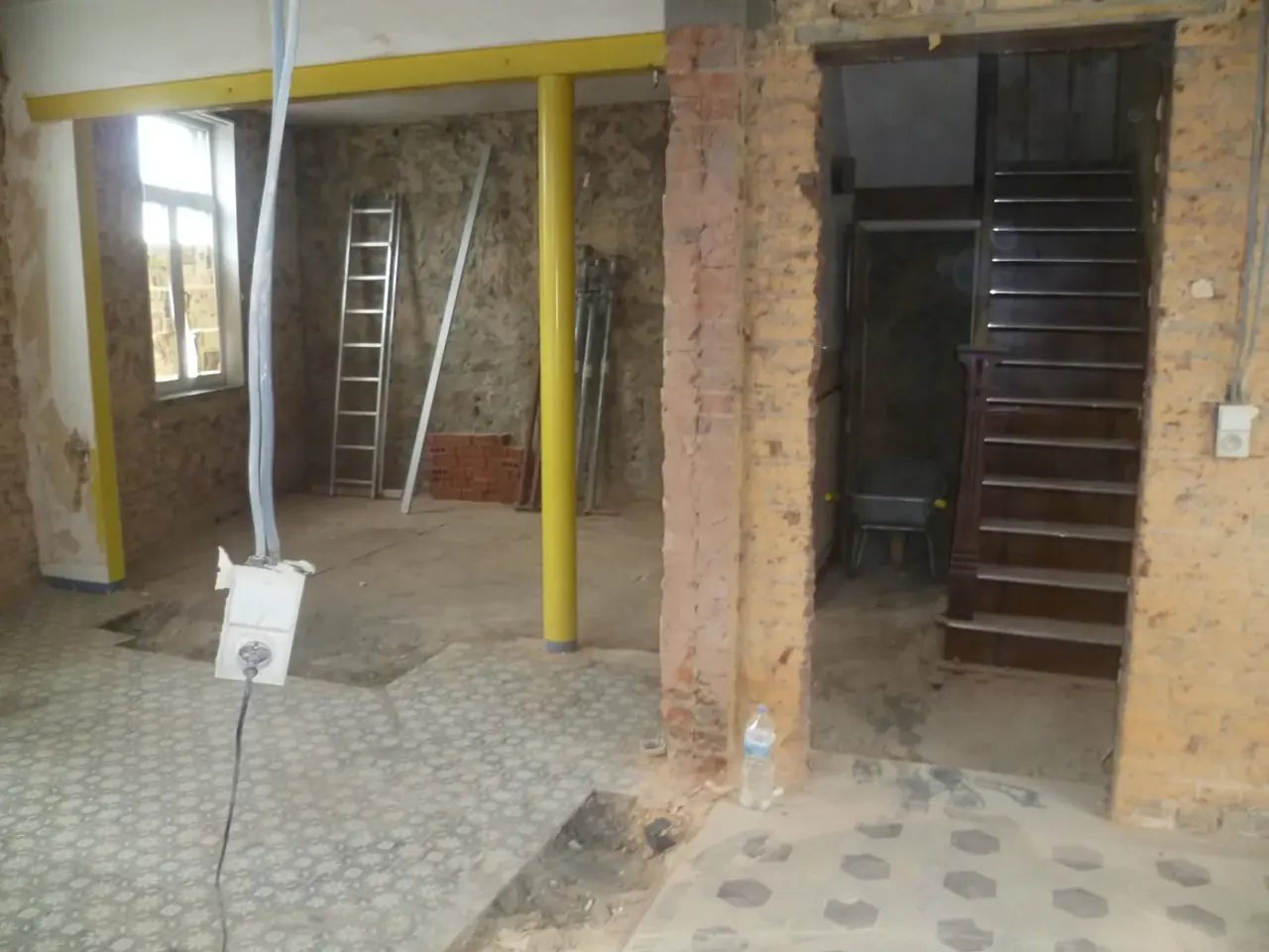 Poteaux métalliques jaunes dans un séjour ouvert et escalier