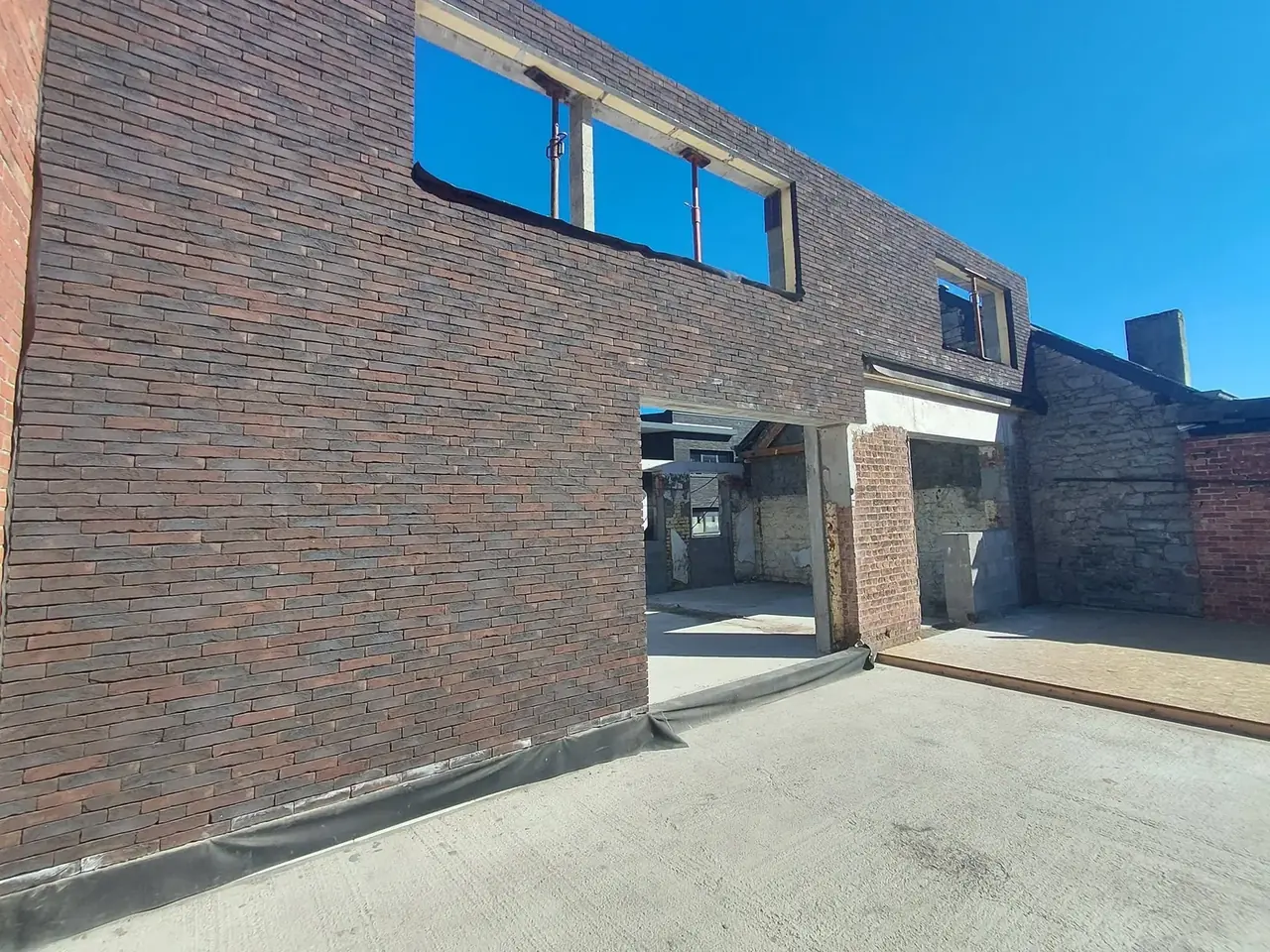 Façade en briques sombres neuves avec fenêtres hautes sous ciel bleu