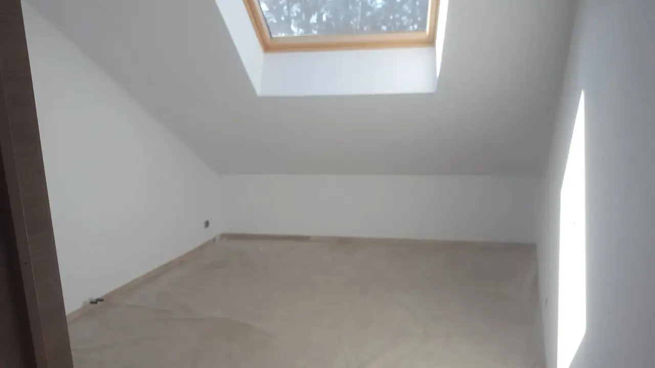 Chambre mansardée aux murs blancs avec fenêtre de toit