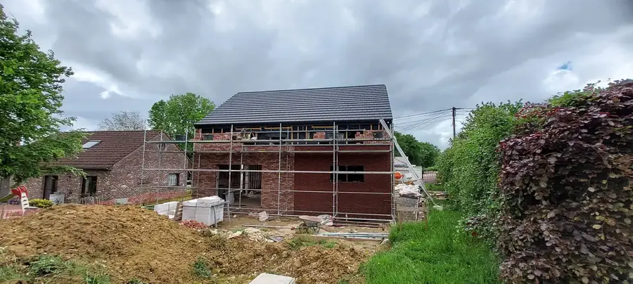 Maison en briques avec échafaudage devant la haie