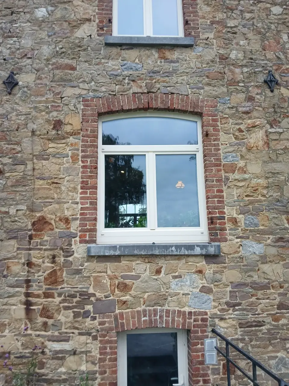 Grande fenêtre blanche encadrée de briques dans une façade en pierre