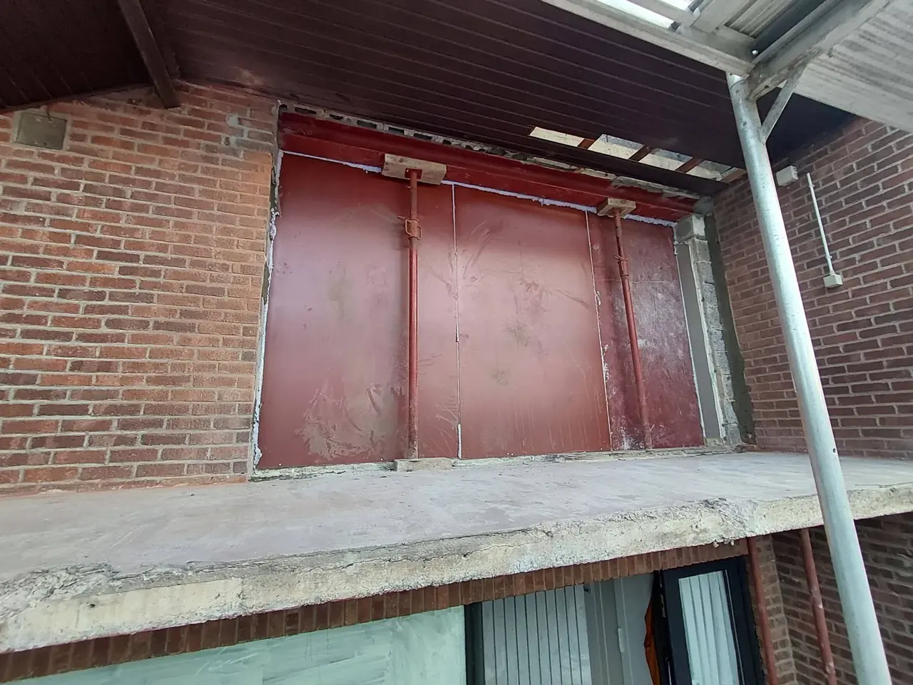 Ouverture protégée par des panneaux rouges sur une façade en briques