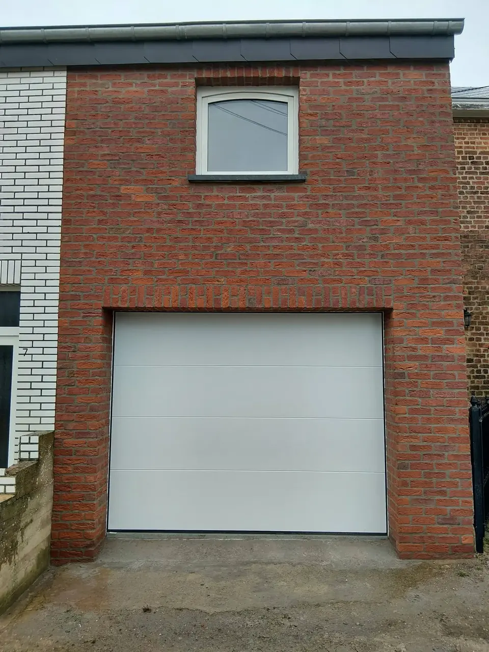 Façade en briques rouges avec fenêtre cintrée et porte de garage blanche