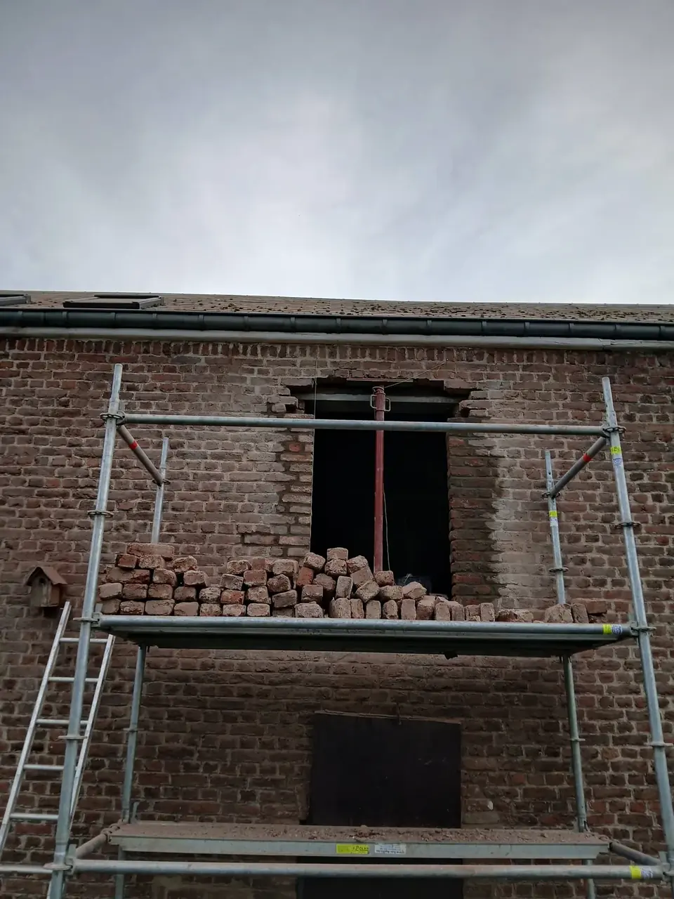 Échafaudage devant une façade en briques avec ouverture et briques empilées