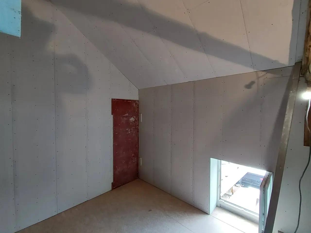 Pièce sous toiture aux plaques de plâtre avec porte rouge et fenêtre