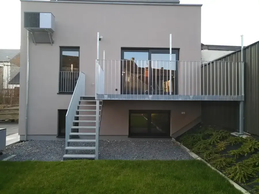 Façade arrière enduite avec terrasse surélevée, escalier et pelouse