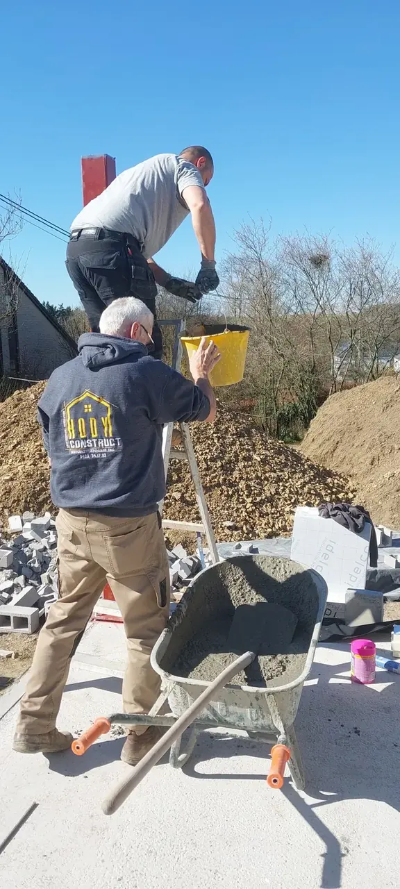 Deux ouvriers de dos qui brouettent du mortier