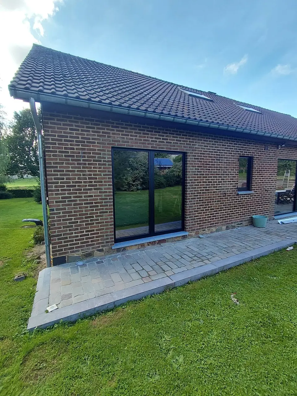 Maison en briques avec baie vitrée noire et toiture en tuiles