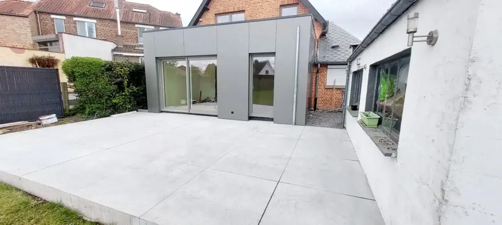 Annexe à façade grise avec baies vitrées et terrasse en béton lissé