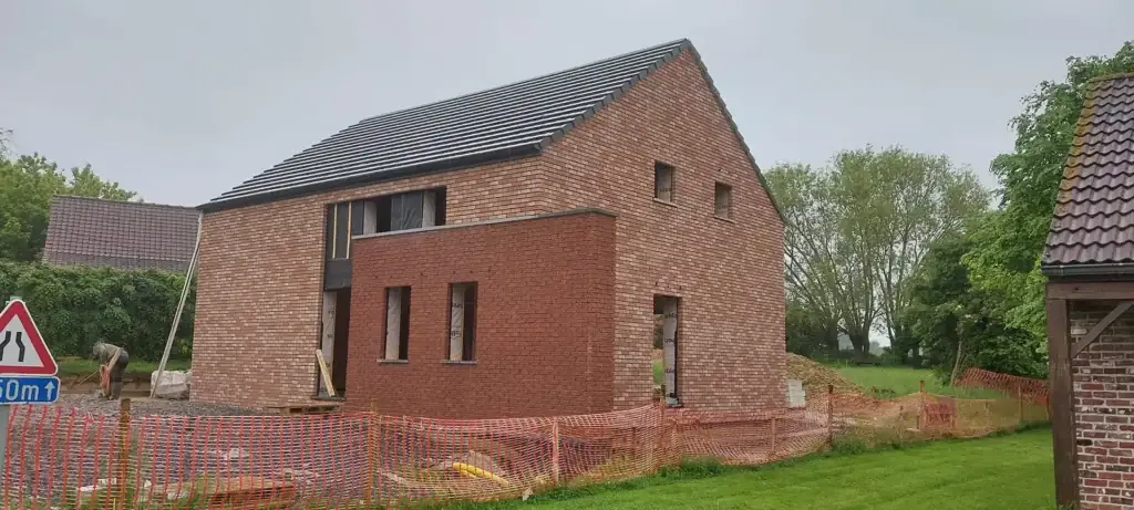 Maison neuve en briques rouges, toiture en ardoise et clôture de chantier