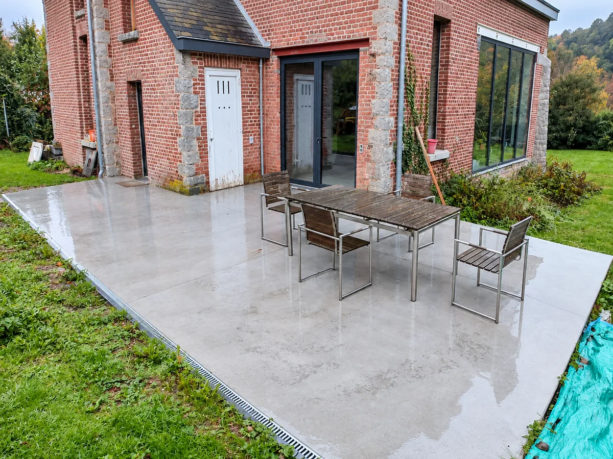 Terrasse en béton lissé avec table et chaises devant une maison en briques