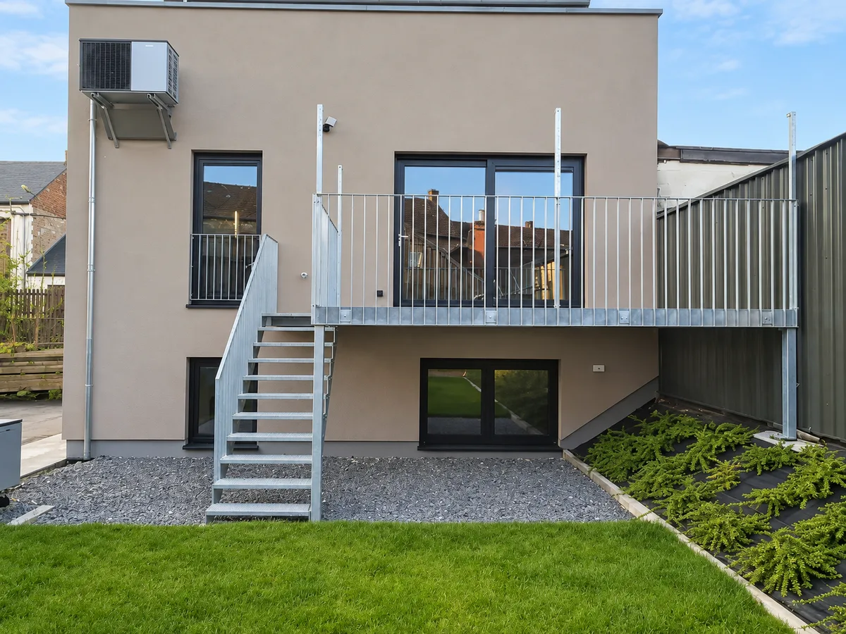 Immeuble neuf au crépi beige avec terrasse, escalier métallique et pelouse